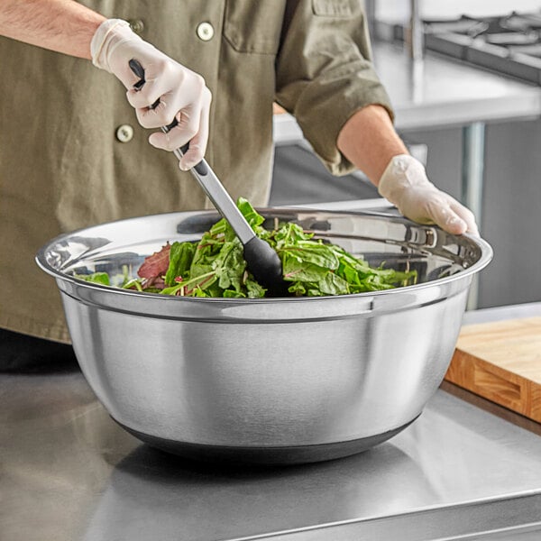 A person mixing greens in a Choice stainless steel mixing bowl.
