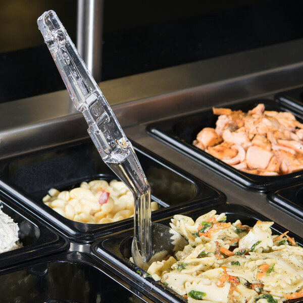 A clear plastic salad bar spoon in a tray of food.