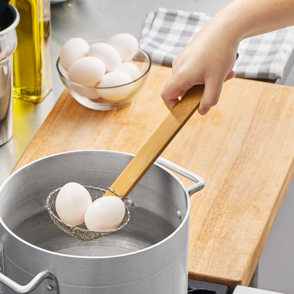 A person using an Emperor's Select wire mesh skimmer to stir eggs in a pot.