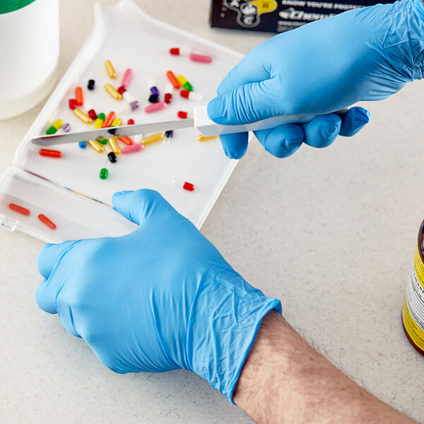 A person in a Showa blue biodegradable nitrile glove cutting pills on a white surface.