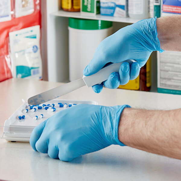 A person in a blue Showa nitrile glove uses a knife to cut something on a counter.