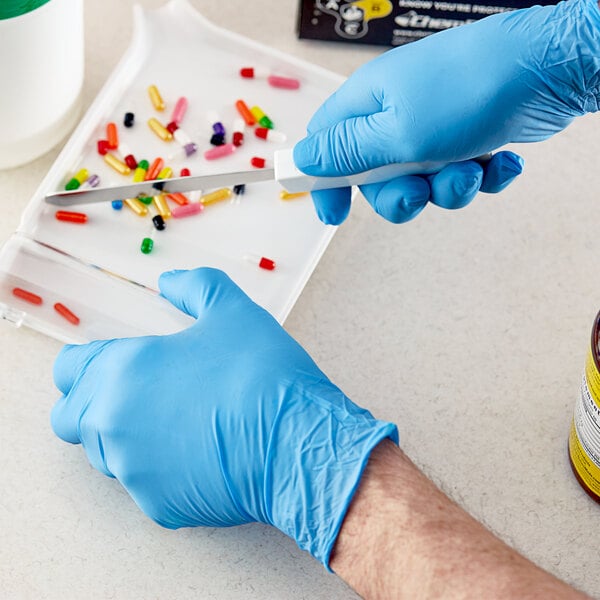 A person wearing a Showa blue biodegradable nitrile glove cuts pills on a white surface.