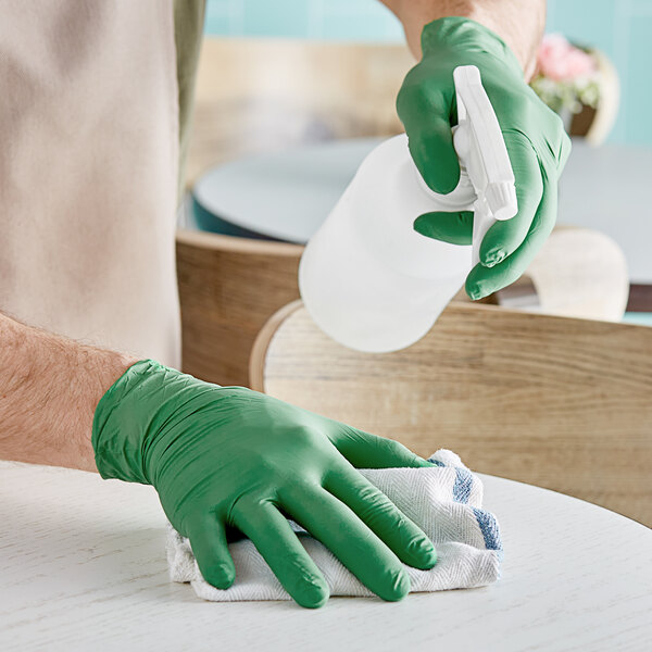 A person wearing green Showa nitrile gloves cleaning a table.