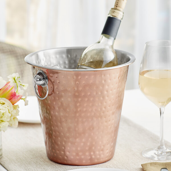 A bottle and glass of wine in a copper wine bucket.