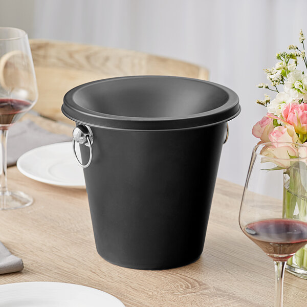 An Acopa black stainless steel wine tasting spittoon on a table.