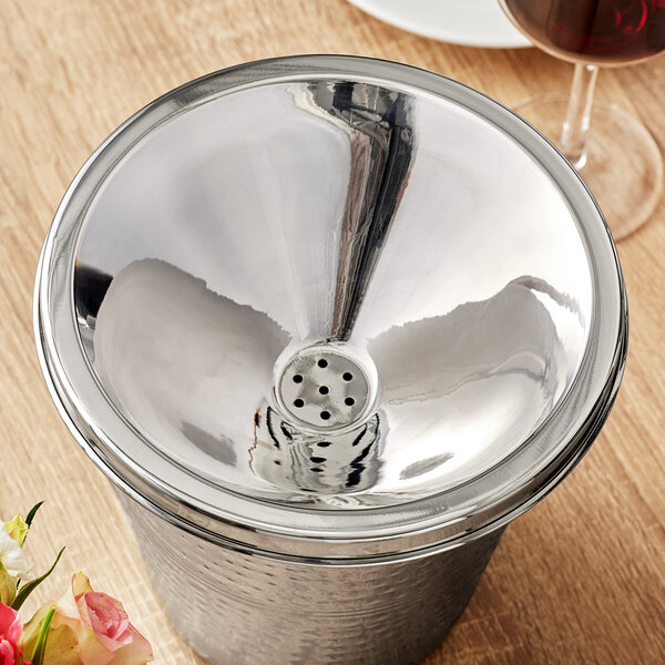 A silver container with Acopa Stainless Steel Wine Tasting Spittoon Lid on a table with a glass of wine.