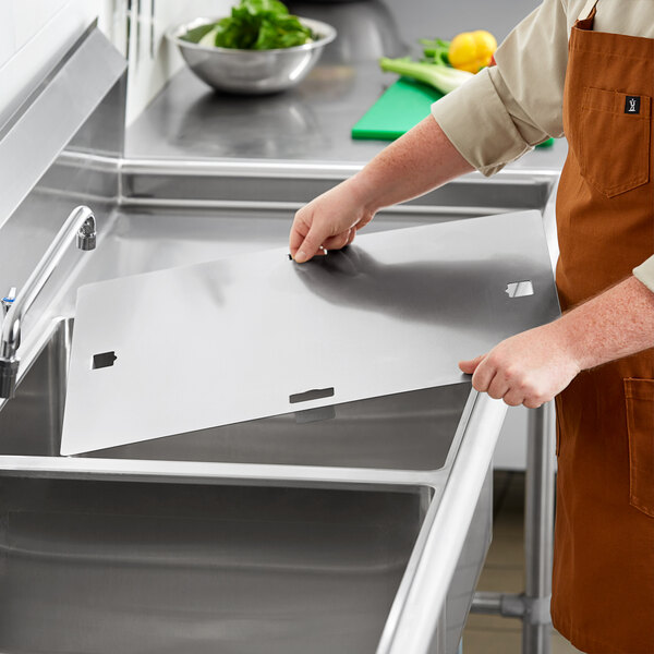 A person in an apron cutting a sheet of metal for a Regency stainless steel sink cover.