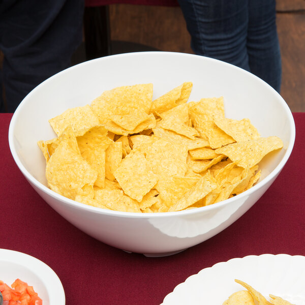 A white round melamine catering bowl filled with chips on a table.