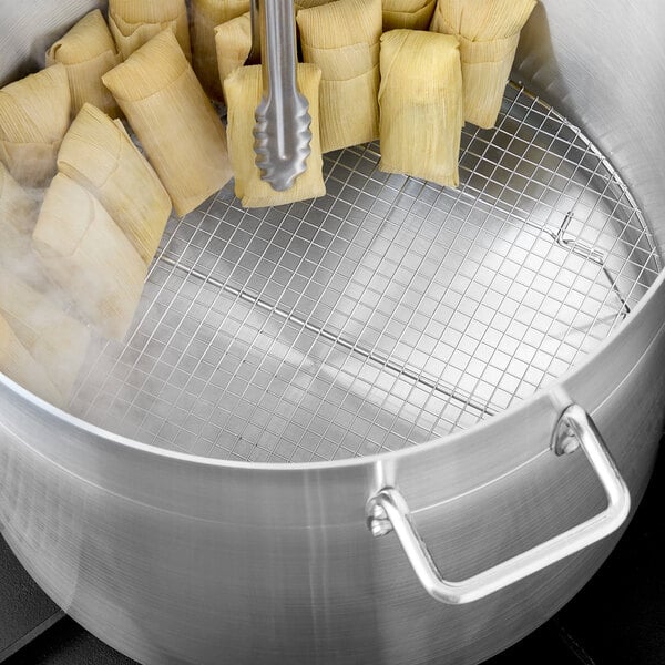 A round silver steamer rack in a pot of tamales.