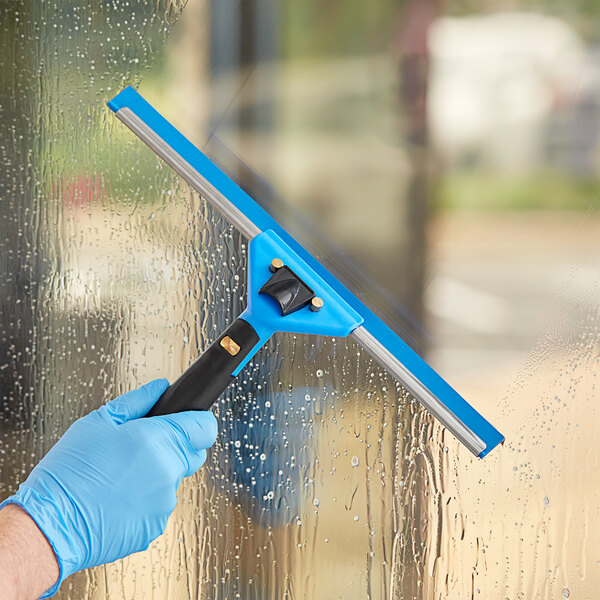 A hand in a blue glove using a Lavex swivel window squeegee with a black handle to clean a window.