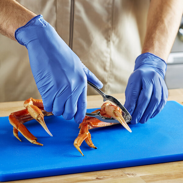 A person in blue Noble NexGen biodegradable nitrile gloves uses tongs to cut a crab claw.