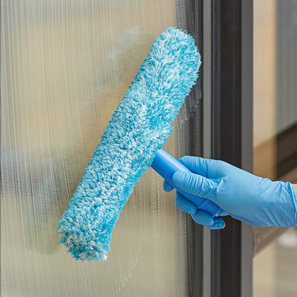A hand in blue gloves using a blue and white fuzzy Lavex Pro strip washer sleeve to clean a window.