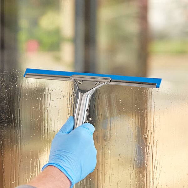 A hand in a blue glove using a Lavex window squeegee to clean a window.