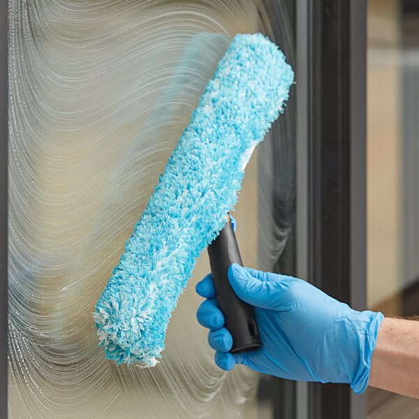 A person in blue gloves using a Lavex window cleaning kit to clean a window.
