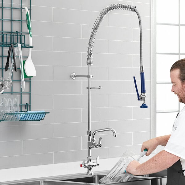 A man using a Waterloo pre-rinse faucet to wash a glass in a sink.