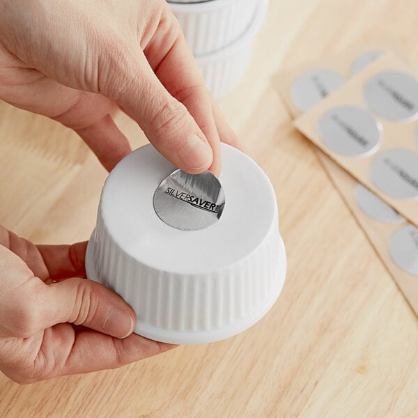 A person putting a silver sticker on a white container.