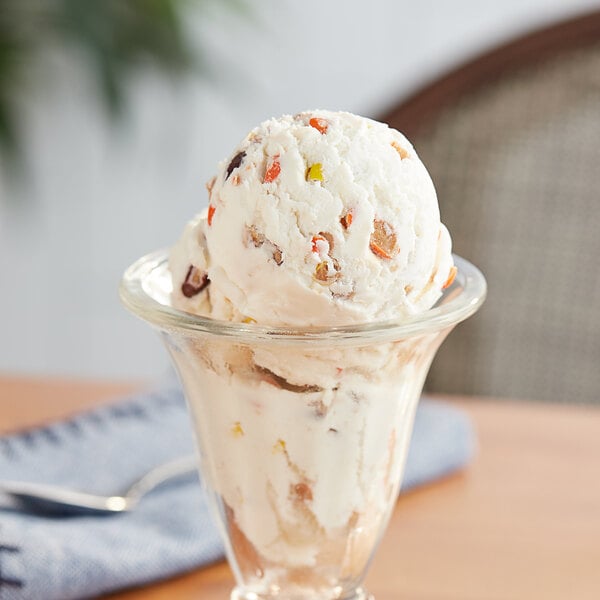 A glass cup with a scoop of ice cream topped with chopped REESE'S PIECES.