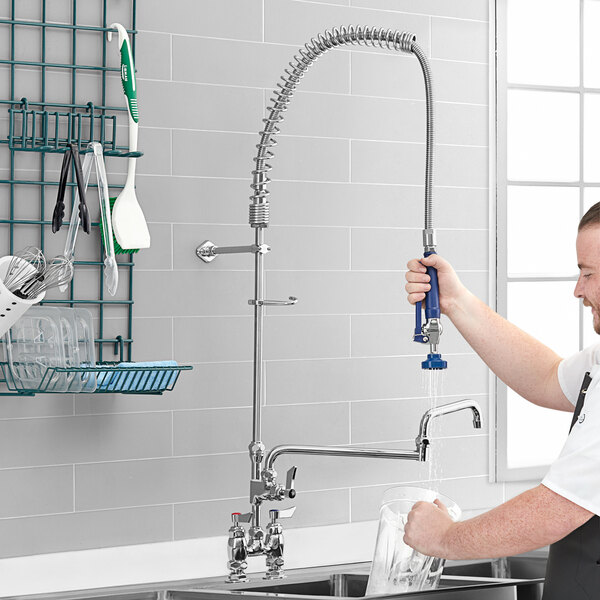 A person washing a glass in a sink using a Waterloo deck-mounted pre-rinse faucet with double-jointed add-on faucet.