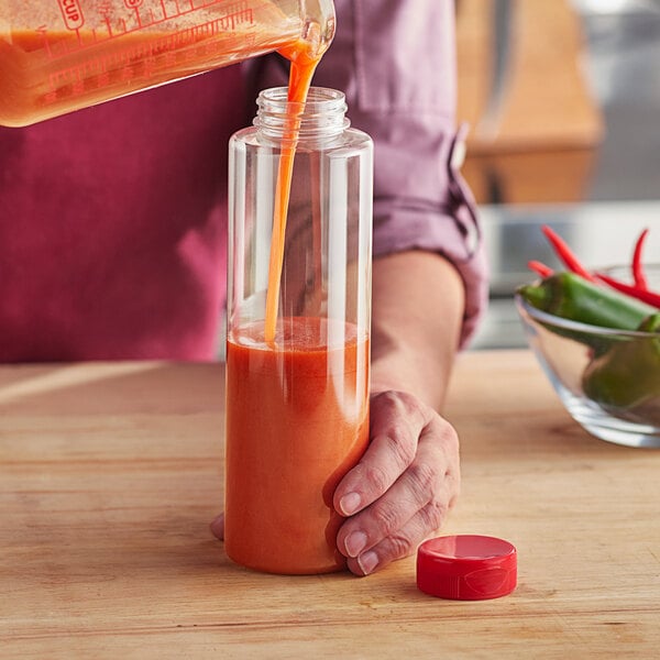 A person pouring orange sauce from a bottle with a red cap into a glass.
