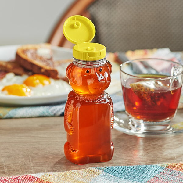 A honey bottle with a yellow lid next to a cup of tea and toast.