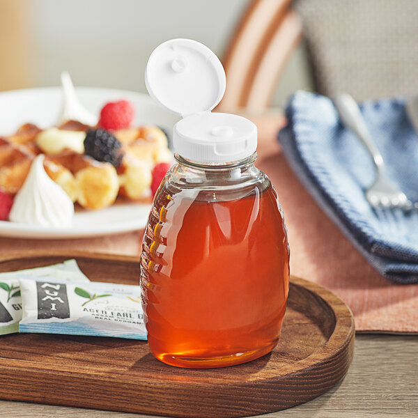 A Classic Queenline PET honey bottle with a white plastic flip top lid on a wooden tray with food.