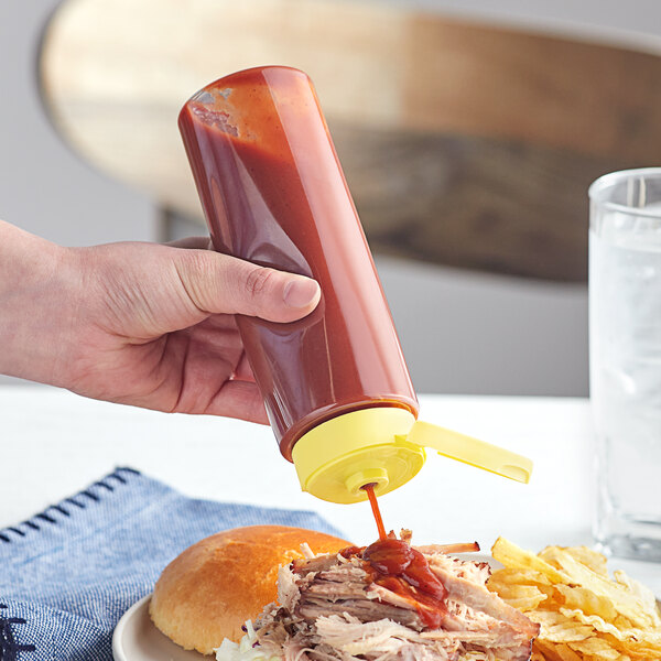 A person using a yellow Cylinder PET sauce bottle to pour sauce on a sandwich on a plate.