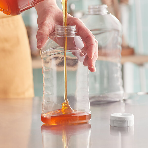 A person pouring honey into a Ribbed Hourglass PET Honey Bottle with a white cap.