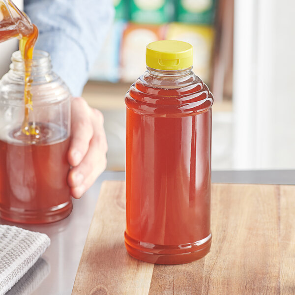 A hand pouring honey into a Skep PET sauce bottle with a yellow flip top lid.