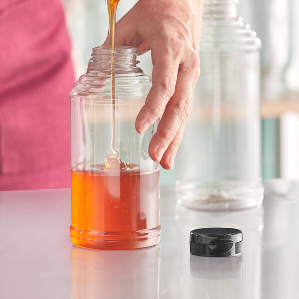 A hand pouring honey into a Skep PET sauce bottle.