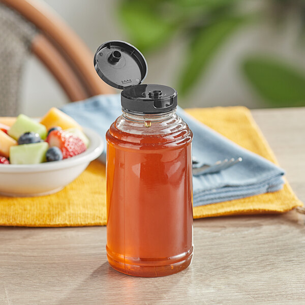 A Skep PET sauce/honey bottle with black flip top lid filled with honey on a table.