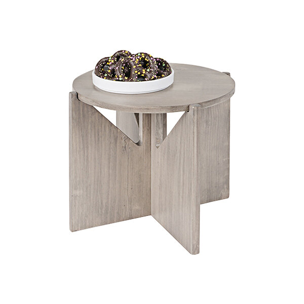 A Cal-Mil round gray-washed pine wood display riser on a round wooden table with a bowl of chocolate donuts on it.