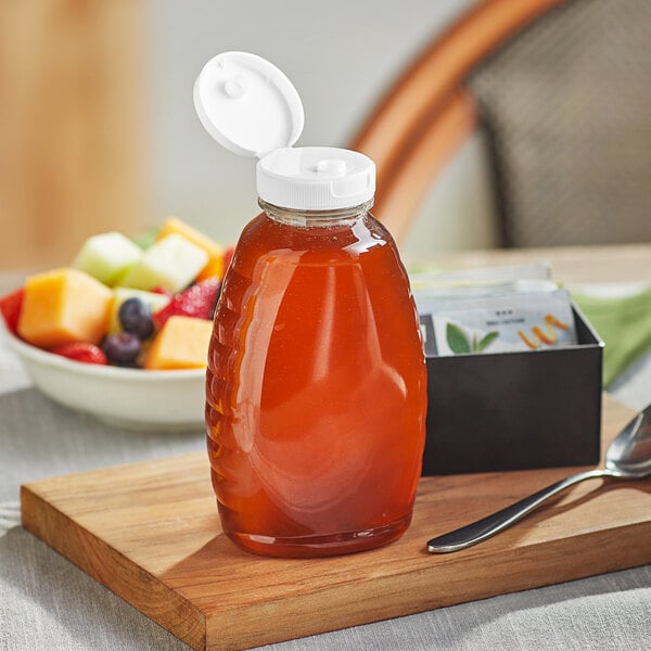 A Classic Queenline PET honey bottle with a white flip top lid on a cutting board with a jar of honey.