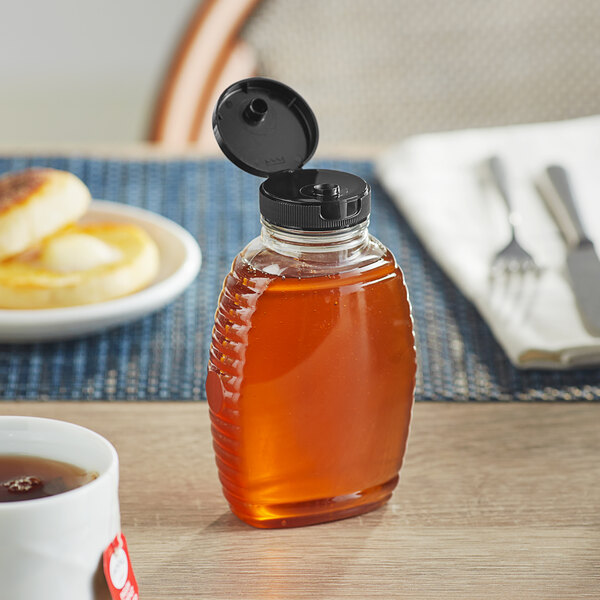 A Classic Queenline PET honey bottle with black flip top lid on a table with food.