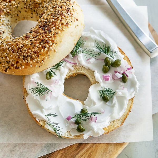 A sesame seed bagel with Violife Just Like Original Cream Cheese spread on it.