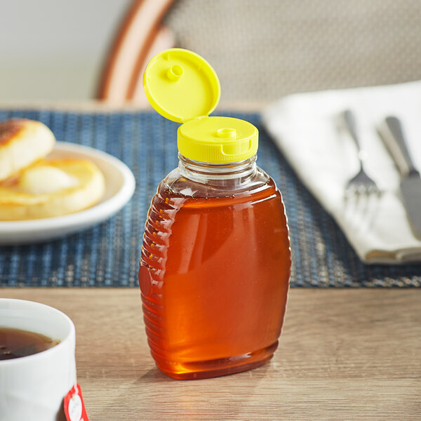 An 8 oz. Classic Queenline PET honey bottle with a yellow plastic flip top lid on a table.