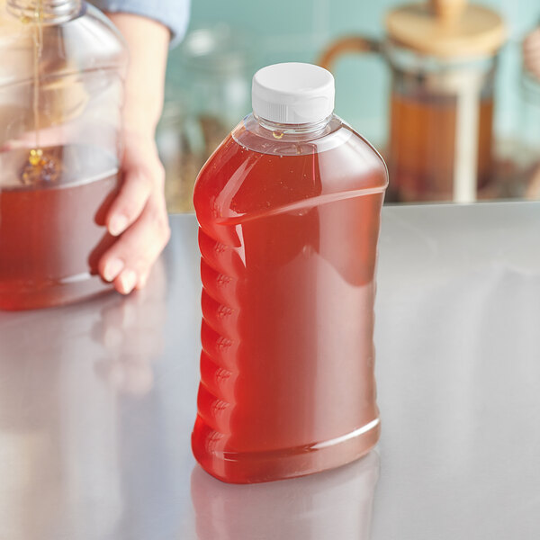 A close-up of a person holding a 27 oz. ribbed hourglass PET honey bottle full of liquid.