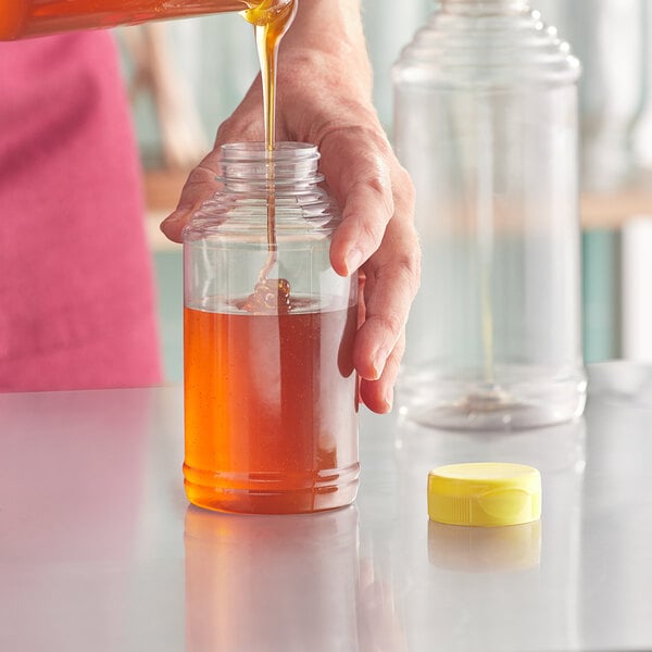 A hand pouring honey into a jar using a yellow Skep bottle cap.