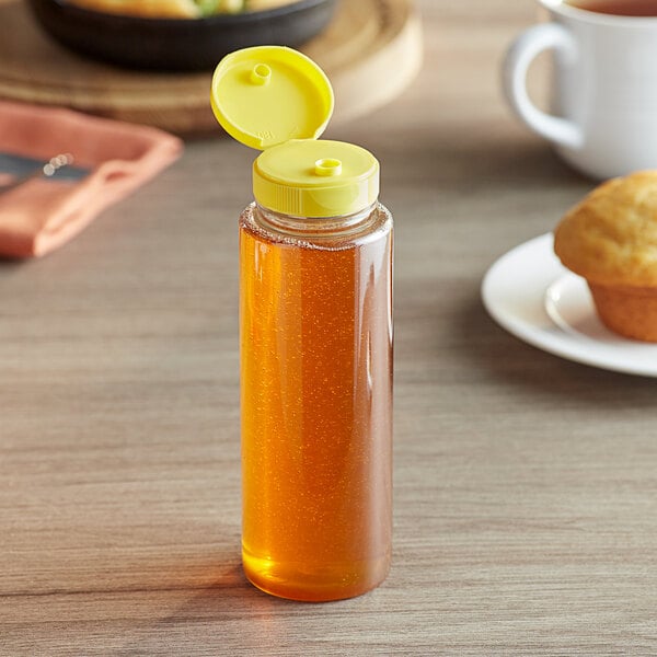 A 8 oz. clear PET sauce bottle with a yellow cap on a table next to a muffin.