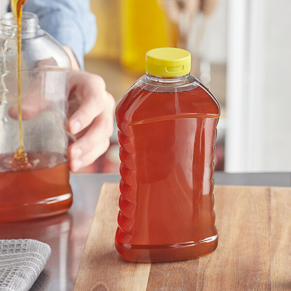 A person pouring honey into a Ribbed Hourglass PET Honey Bottle.