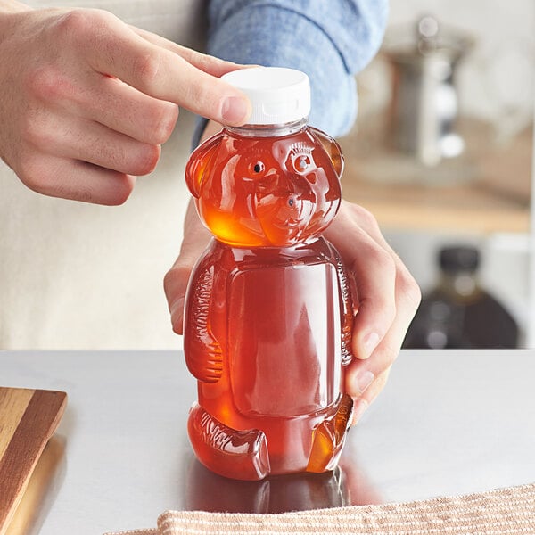 A person pouring honey into a bear-shaped honey bottle.