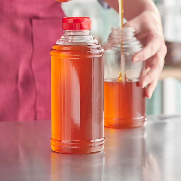 A person pouring honey into a Skep PET sauce bottle with a red cap.
