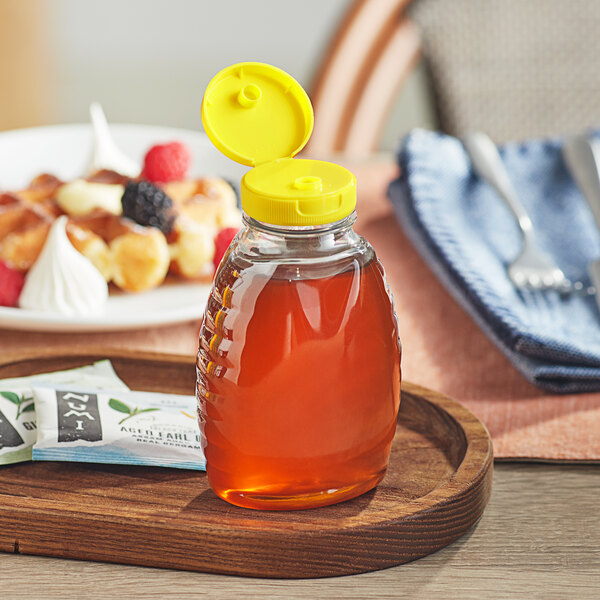 A Classic Queenline PET honey bottle with a yellow flip top lid on a plate of food.