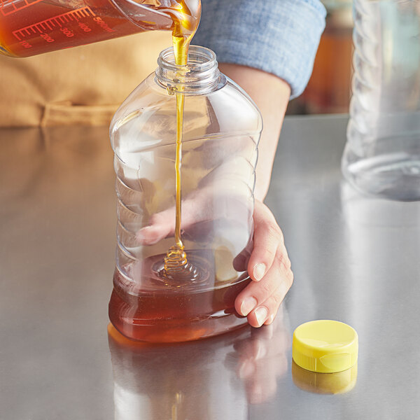 A person pouring honey into a Ribbed Hourglass PET plastic bottle.