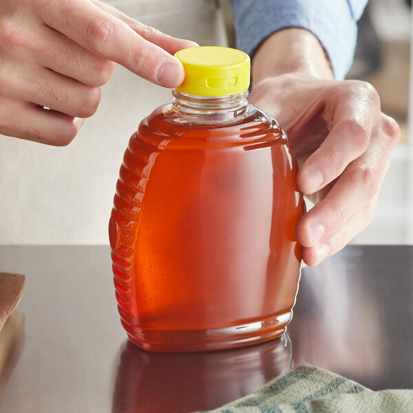 A hand holding a Queenline PET plastic bottle of honey
