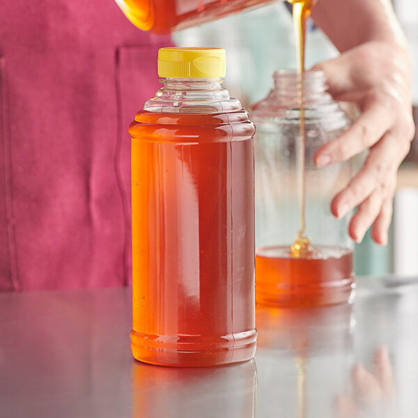 A hand pouring honey into a Skep PET sauce bottle with a yellow cap.