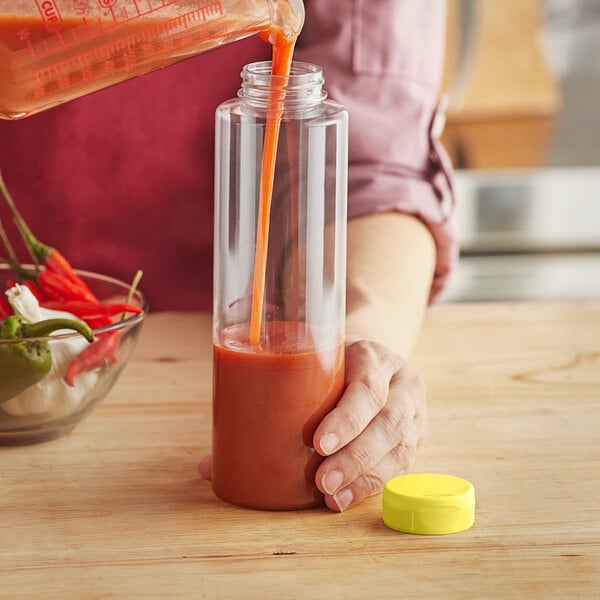 A person pouring sauce into a clear sauce bottle with a yellow cap.
