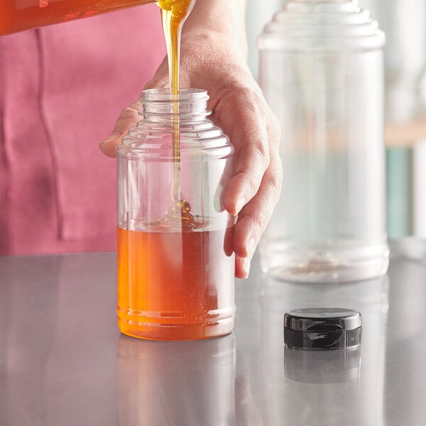 A hand pouring honey from a Skep bottle into a glass jar.
