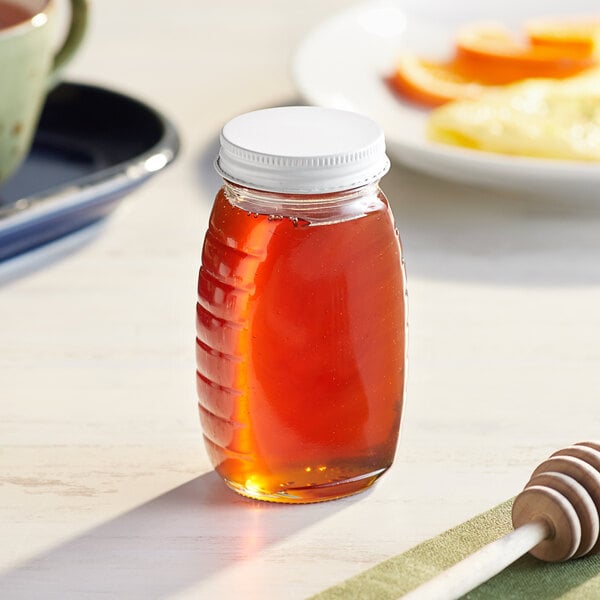 A Classic Queenline glass jar of honey with a white metal lid on a table.