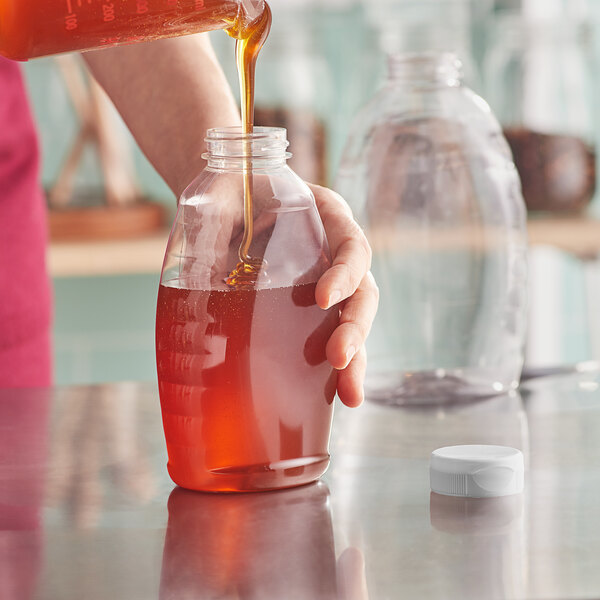 A person pouring honey into a Classic Queenline PET Honey Bottle.