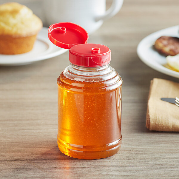A bottle of honey with a red cap on a table.